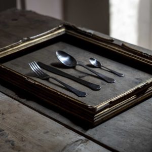 cornice di quadro appoggiata su un tavola che incornicia il set di posate