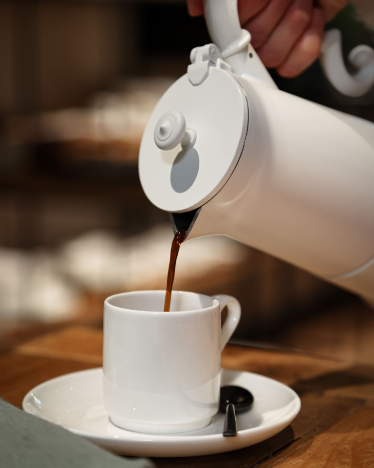 dettaglio caffettiera bianca che versa caffè in tazzina bianca